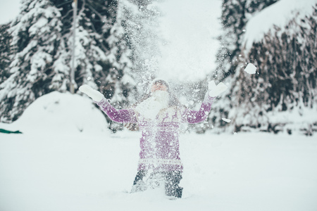 Beautiful young brunette scatters the snow into white clouds and smiles while playing in winterの写真素材