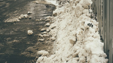 Interesting composition made of metalic white fence and dirty snow humpsの写真素材