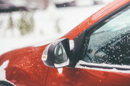 Red car is covered with winter fluffy snow, closeup of mirror and side window is captured on the photoの写真素材