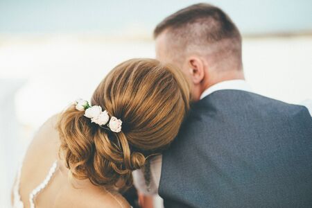 The bride laid her head on the groom's shoulder. Her hair is decorated with white flowers. Back view.の写真素材