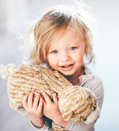 Close up shot of a nice blonde blue eyed girl holding a plush toy in her hand and smiling innocentlyの写真素材