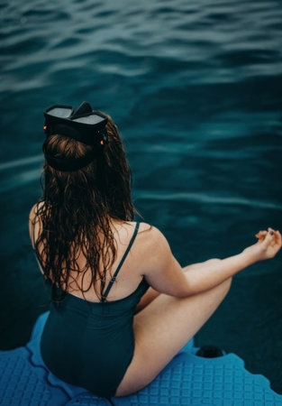 Blurred girl sits in a turquoise bathing suit on a pier near the water in a diving mask and...