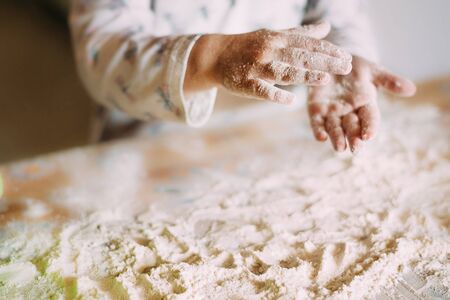  Blurred hands of a little girl who prepares the dough for baking and everything around is in flour. Flour on the table flies from the hands of a child.の写真素材