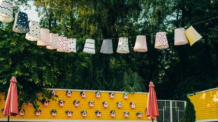 Close-up of paper cardboard holiday decorations hanging over a yellow brick wall in a forest. Pink birdhouses on the wall.の写真素材