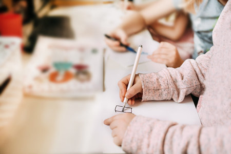 A little girl next to her brother sits at home draws on paper with a felt-tip pen and a pen during...