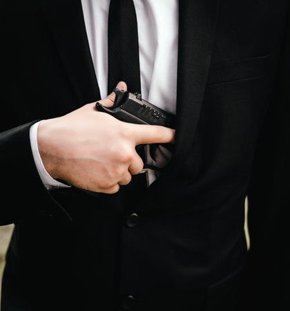 Close up blurred hand with a gun of man in a suit, jacket and white shirt, black tie.