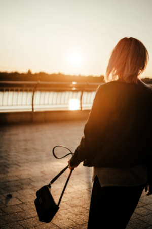Beautiful young woman walks towards sunrise with a handbag in the city.の写真素材