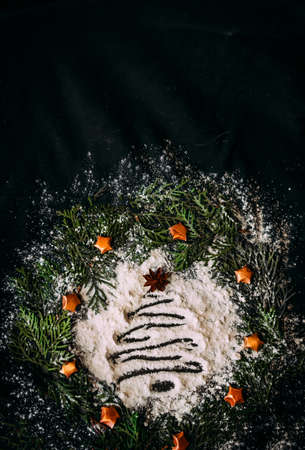 The figure of a Christmas tree made of flour on a black background in a frame made of fir branchesの写真素材