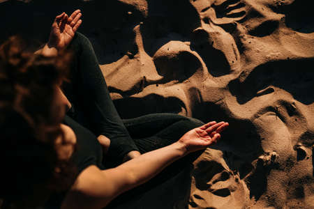 Yoga background. The girl is sitting on the beach in the lotus position. No face, only arms, legs, sand. Meditation, balance, life balance, pacification, relaxationの写真素材