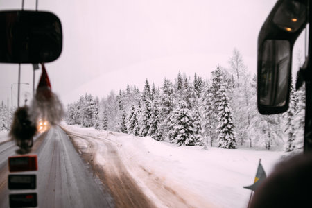 Snowy dense forest covered with snow and a road. View from the front window of the busの写真素材