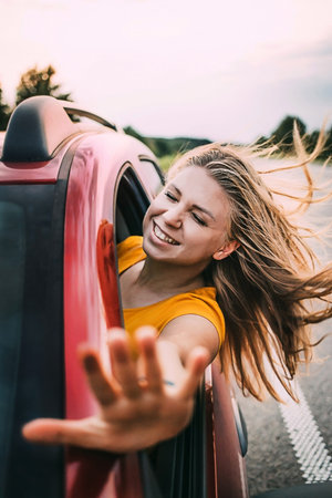 A woman pulls her hand out of the car and smiles, the wind blows her hair