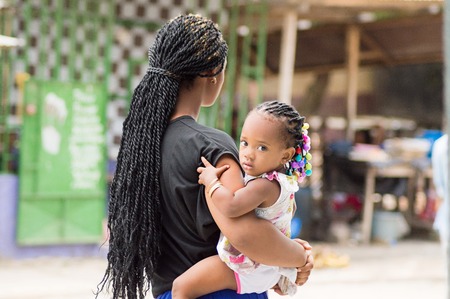 Abidjan March ivory coast in September 2015 a young woman with her baby and her braids while on the back the baby 39s eyes fixed on the camera.This young woman walking down the street with her baby on the side as the african womenhave the coat.のeditorial素材