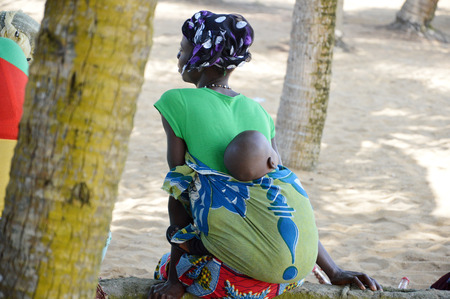 Abidjan, Ivory coast - August 29; 2015: a yong woman, tied her head with a scarf, her baby sleeping in her back, sat under a coconut tree Taking a rest.のeditorial素材