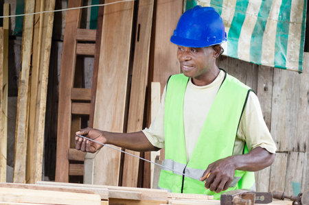 The plane On His desk, the carpenter holds in His Hands measurement tool to measure His boarbsの写真素材