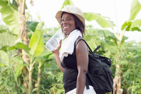 This smiling young woman holding a bottle of mineral water, carrying a bag on her back on her returned to town after-Alate sports trainingの写真素材