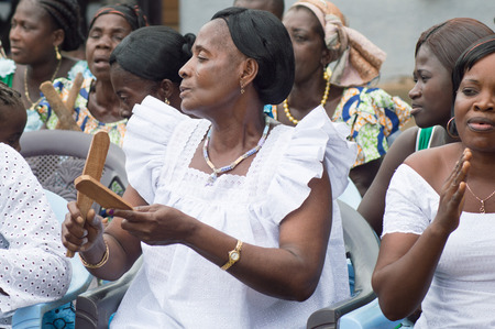 Anekro, Ivory Coast - 21 August 2015: Women typing traditional musical instruments .A woman aged in the foreground in white comisole, tape two pieces of wood and flat back --other women making the foreground as Samiのeditorial素材