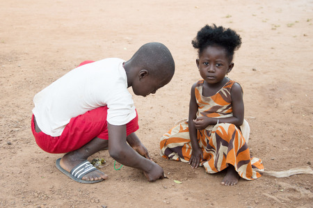 Anekro, Ivory Coast - August 20, 2015: Two children play in the street, the two crouched, hands on the floor and the little girl looks at the cameraのeditorial素材