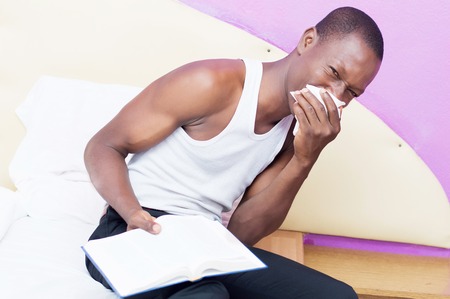 this young man sitting on a bed and holding a bible Suffering from a coldの写真素材