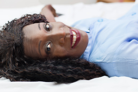 Smiling young woman lying on her bed and looks at the camera at home.の写真素材
