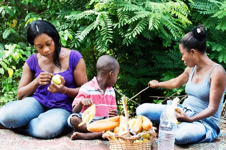 Two young women sitting with a child and a basket of food before themの写真素材