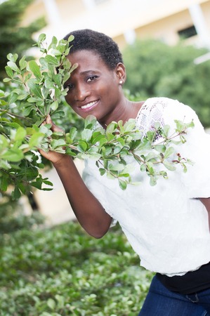 Smiling young woman hidden behind foliage looks through.の写真素材