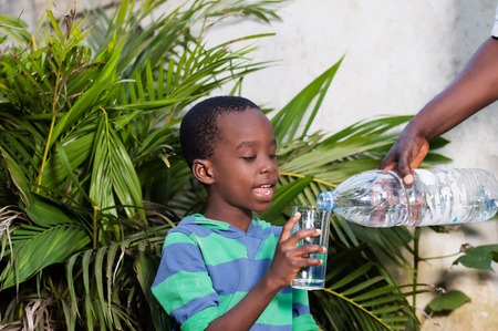 smiling little boy holding a glass of water in which they serve him water.の写真素材