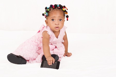 Pretty baby sitting and playing with his mother's mobile phone, isolated on a white backgroundの写真素材