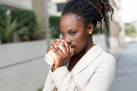 Young businesswoman standing outside and drinking coffee.の写真素材