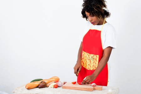 Young cook standing in front of a table, cutting tomato on a piece of woodの写真素材