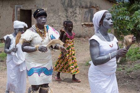 adzopÃ©, Ivory Coast -August 31, 2016: Young woman dressed in traditional dress necklaces with arm powder bracelets on the body walking between two others holding in hand ponytail.のeditorial素材