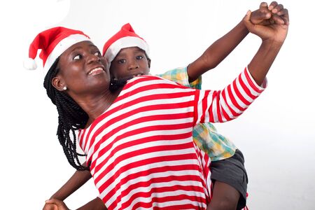 child on the back of his mother with Santa's hats both look in the same direction with outstretched arms.の写真素材