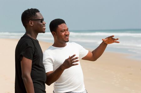 two young people standing at the beach one in black tee shirt and the other in white shirt talking.の写真素材