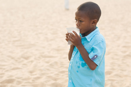 little boy standing in blue shirt drinking water in plastic.の写真素材