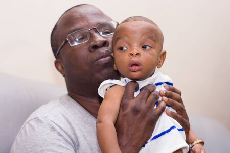 father and baby having fun at home. Proud African father holding an infant in arms while playing.の写真素材