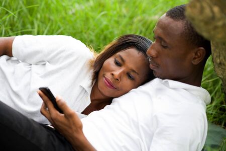 happy couple lying in the grass having fun outdoors on a mobile phone.の写真素材