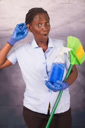 Young cleaning lady listening to novelty wears gloves and holds in hand a brush and a bottle of cleaning productの写真素材