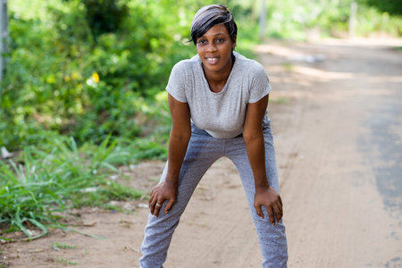 Tired woman runner resting after running hard on the road in the forest leaning forward resting her...