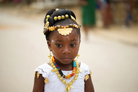 Abidjan, Ivory Coast - February 13, 2018: Portrait of an unidentified girl dressed in white camisole wearing necklaces and pearls in the hair of the street.のeditorial素材