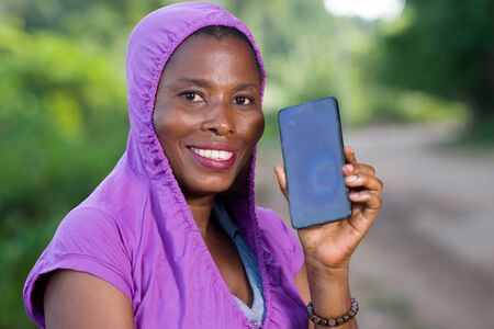 young woman standing in purple dress showing her mobile phone while smiling.の写真素材