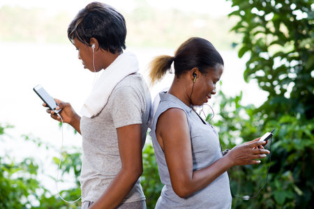 Standing young women are watching their cell phones while giving themselves backs.の写真素材
