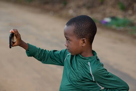 portrait of a child photographing himself with a mobile phone on a road.の写真素材