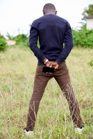 man standing in the grass with his hands crossed in the back and holding a mobile phoneの写真素材