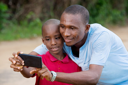 Father and son taking photo with smart phone together outdoor. Family selfie time.