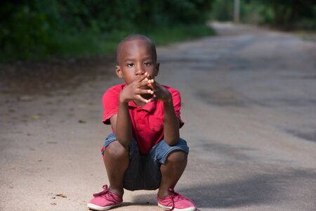 little boy in red t-shirt squatting on a lane and looking at the camera.の写真素材