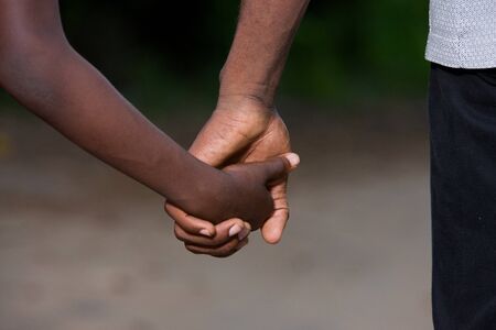 father and little son holding hands walking on a road. the father's hand lead his son into the wild with confidence in the outdoors protecting him.the parental concept of parental care. road to life.の写真素材