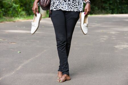 Legs of black pants woman standing on a road with shoes in hands.の写真素材