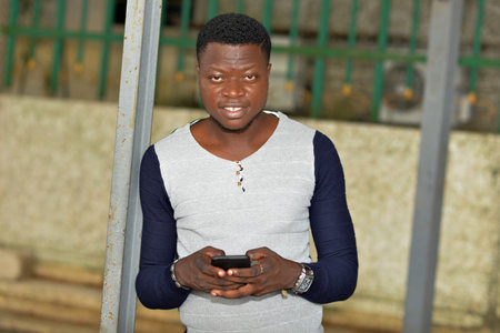 portrait of smiling young man handling a smart phone on the street while looking at the camera