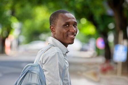 young man standing with backpack looking at the camera smiling.の写真素材