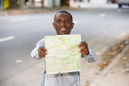 young man in shirt standing with map and smiling on camera.の写真素材