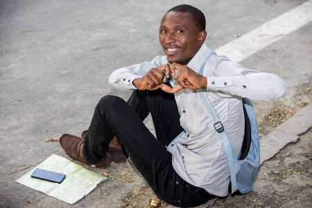 young man sitting on the ground backpack watching the camera smiling.の写真素材